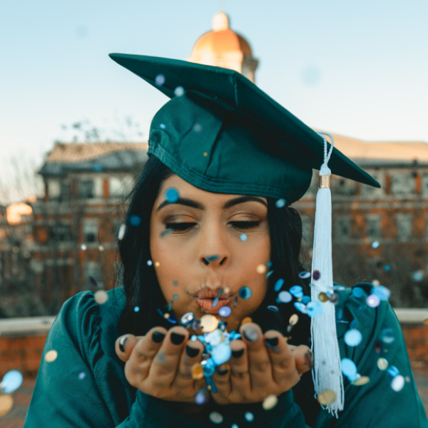 Graduating student in cap and gown blowing confetti